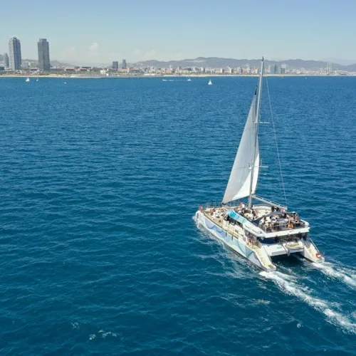 Sailing catamaran on blue water beside the Barcelona coastline