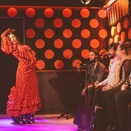 Flamenco dancer in a red polka-dot dress with guitarists at Los Tarantos