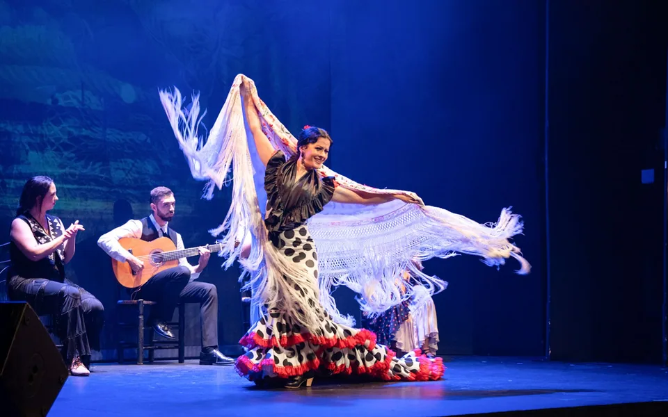 Flamenco dancer with a white fringed shawl beside a guitarist